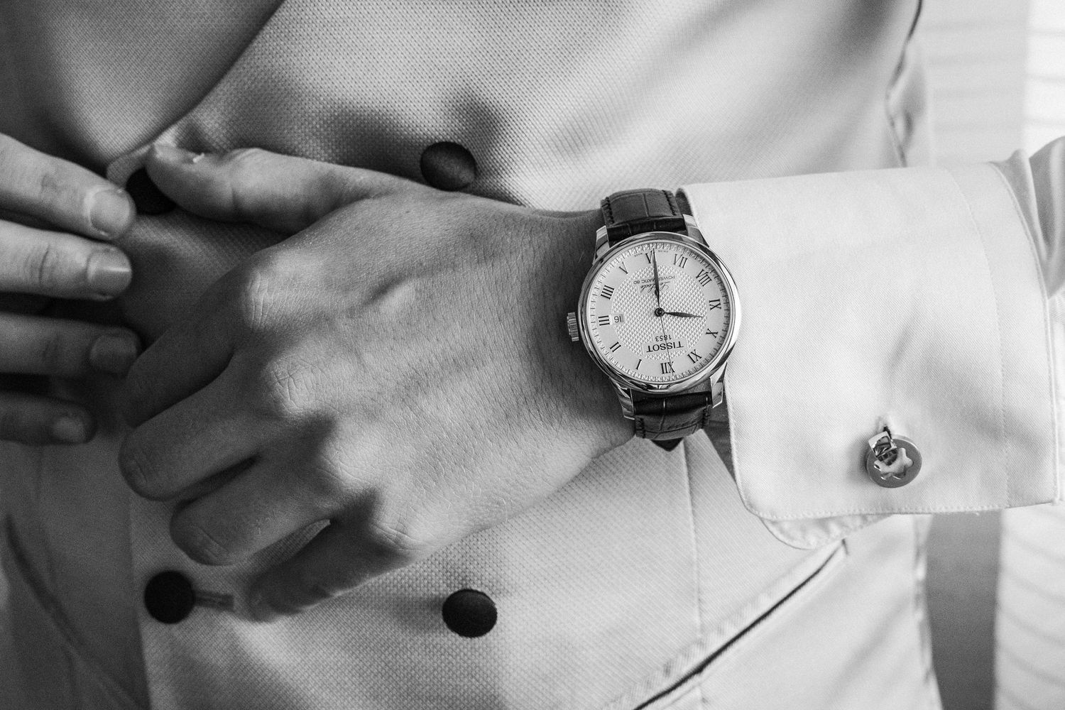 Close-up detail of a classic wristwatch and formal shirt cuff with cufflink.