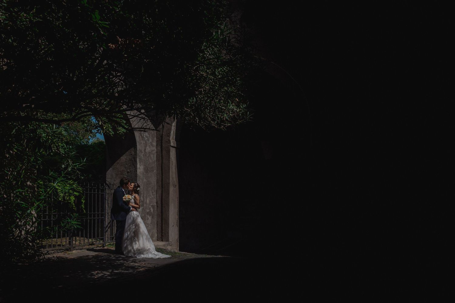 Artistic wedding photo with couple illuminated in dramatic spotlight against dark surroundings.