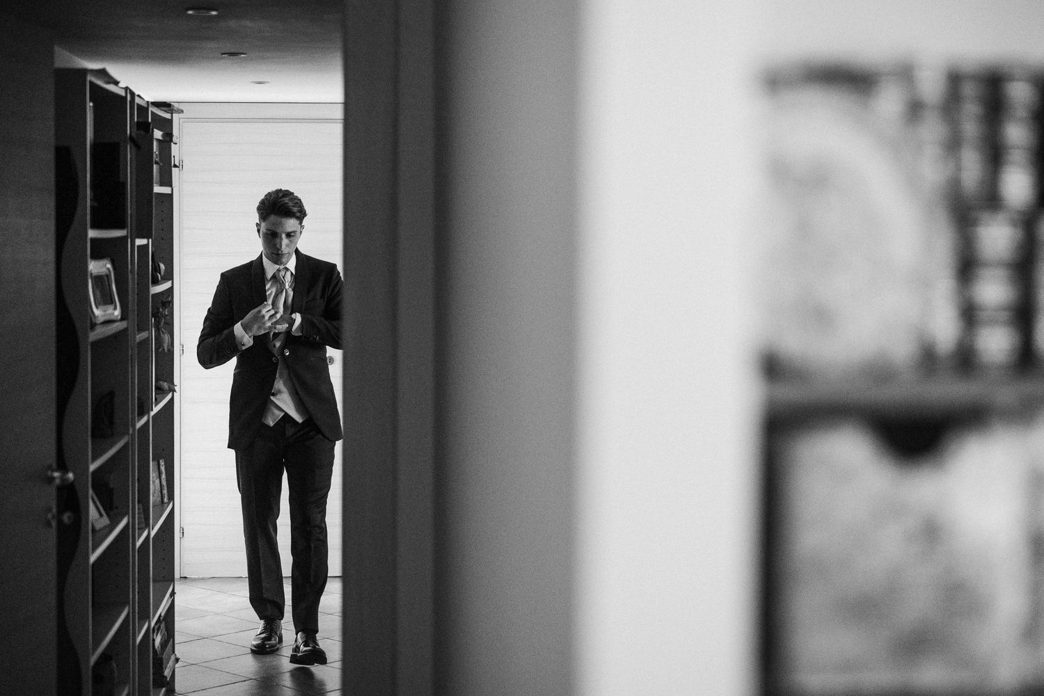 A silhouetted figure in formal wear walks through a hallway with bookshelves.