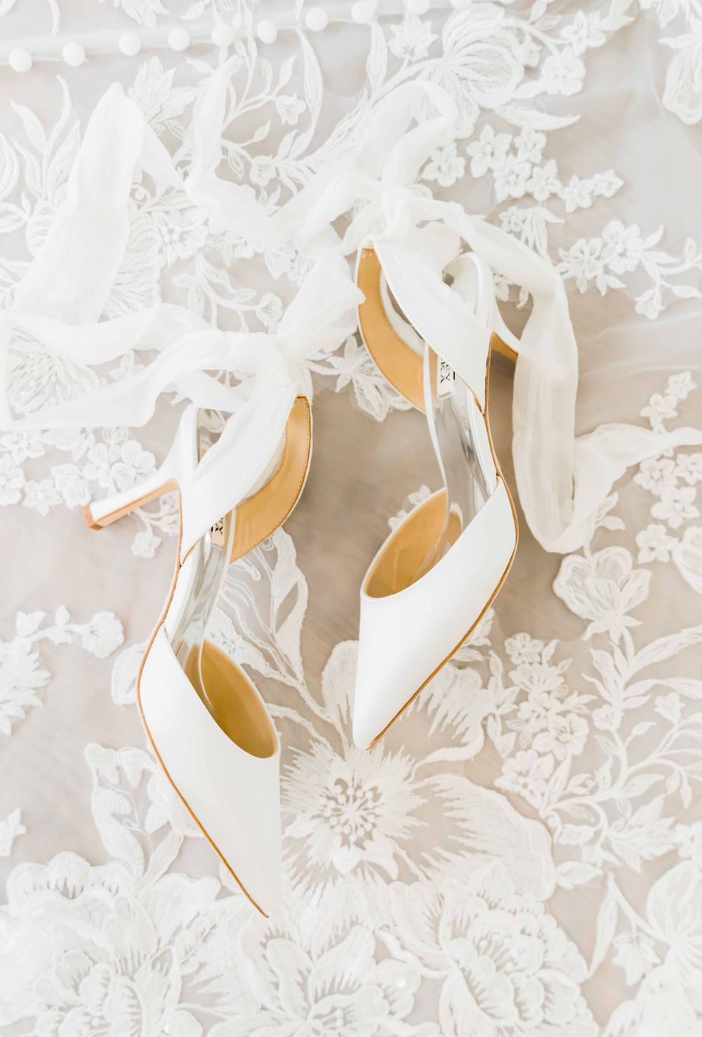 White bridal heels photographed on delicate lace fabric with floral patterns.