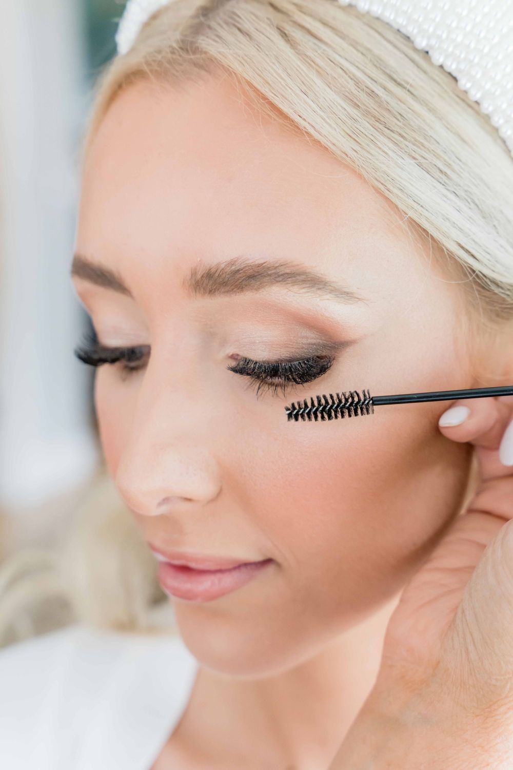 Close-up of eye makeup application with mascara brush creating dramatic lashes for bridal beauty look.
