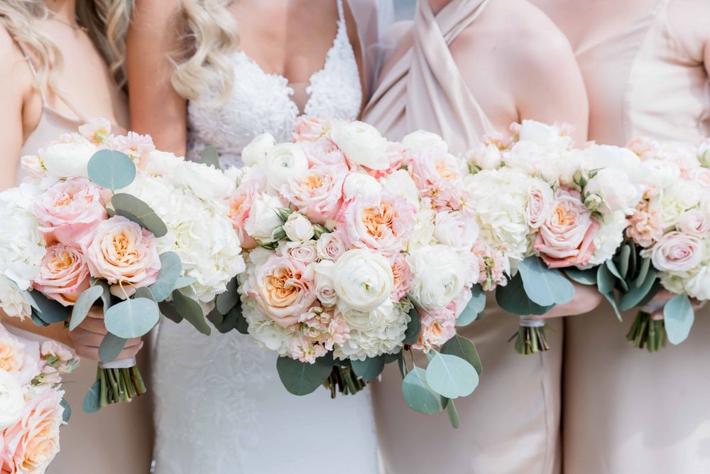 Row of matching pastel pink and white wedding bouquets with roses and eucalyptus.