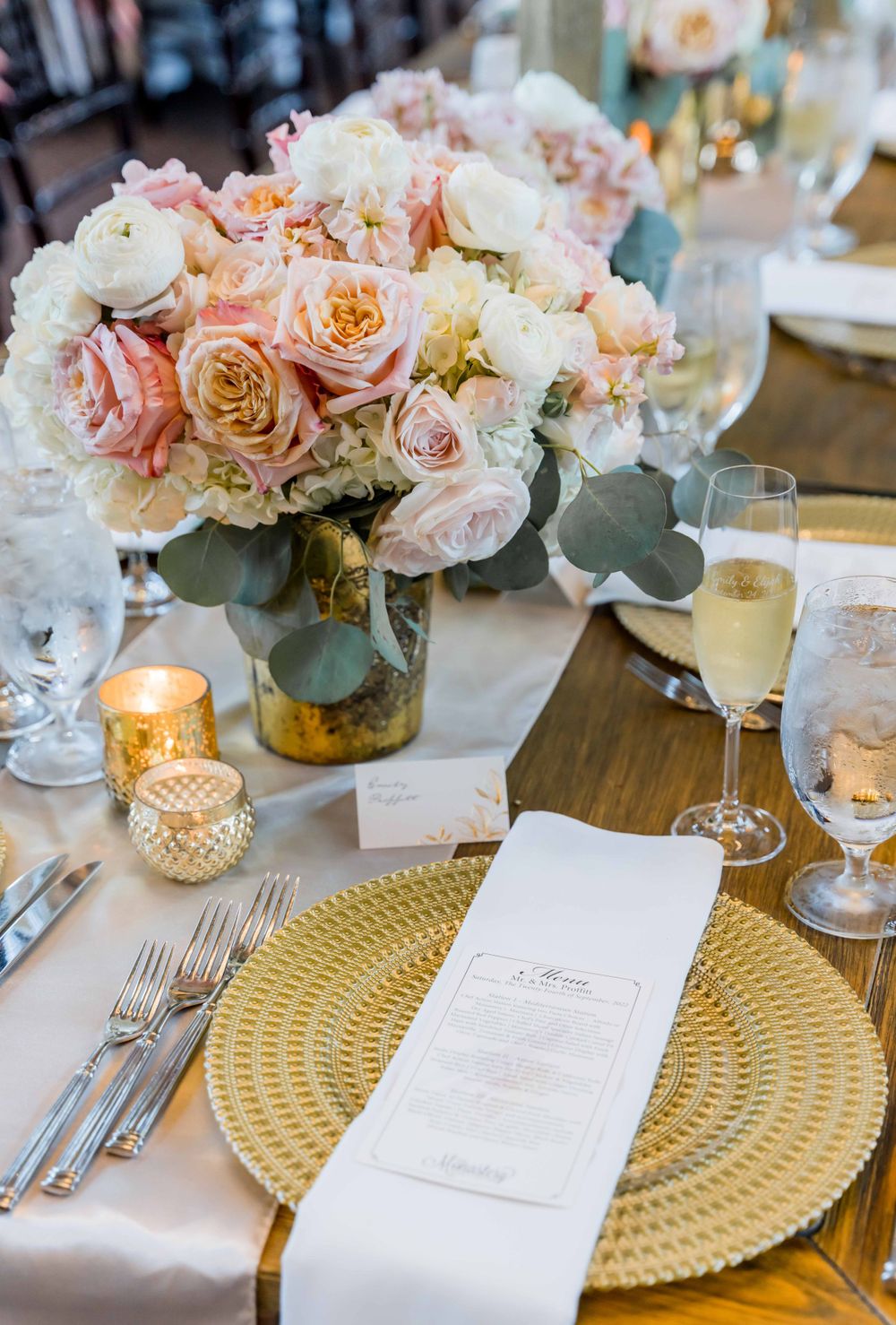 Elegant wedding table setting with pink and white roses, gold charger plate, and candlelight centerpiece.