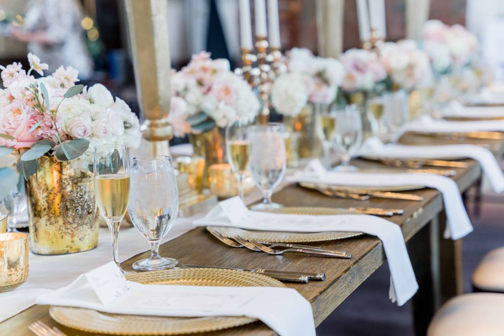Wedding reception table with blush floral centerpieces, gold chargers, and champagne glasses.