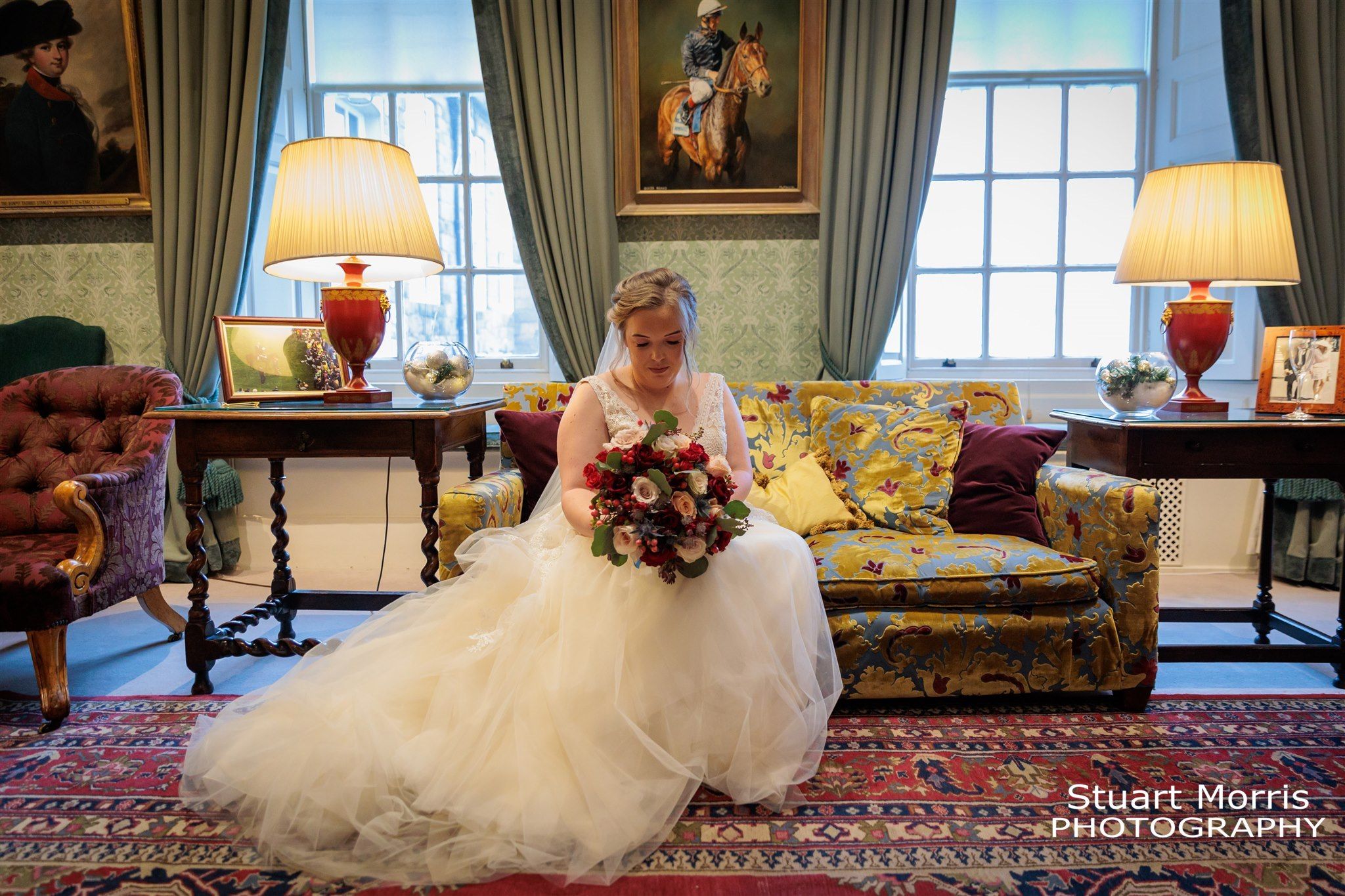 Brides sits on a couch looking at her bouquet in one of the rooms at Knowsley hall