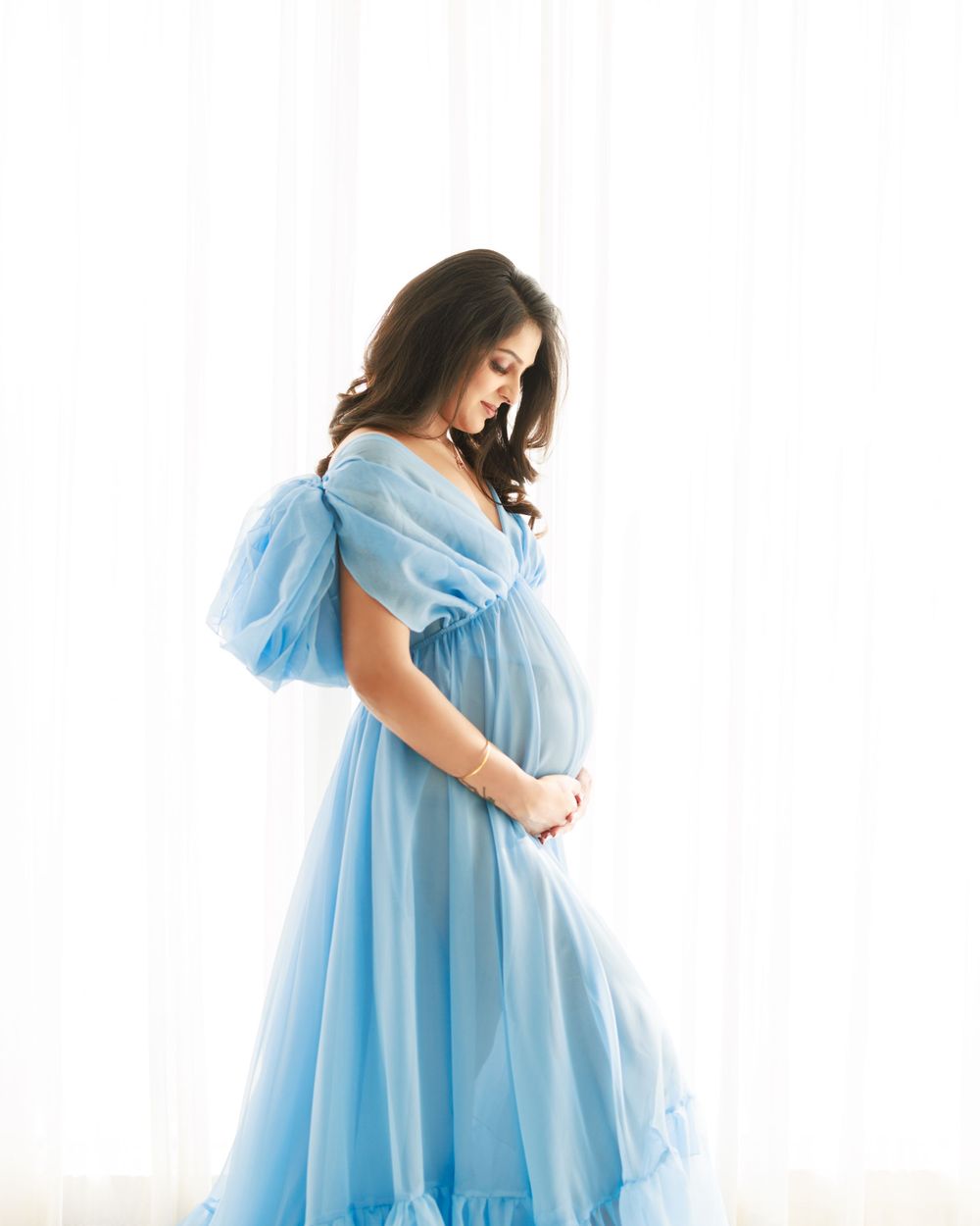 Side view maternity portrait in light blue tulle dress against bright background.