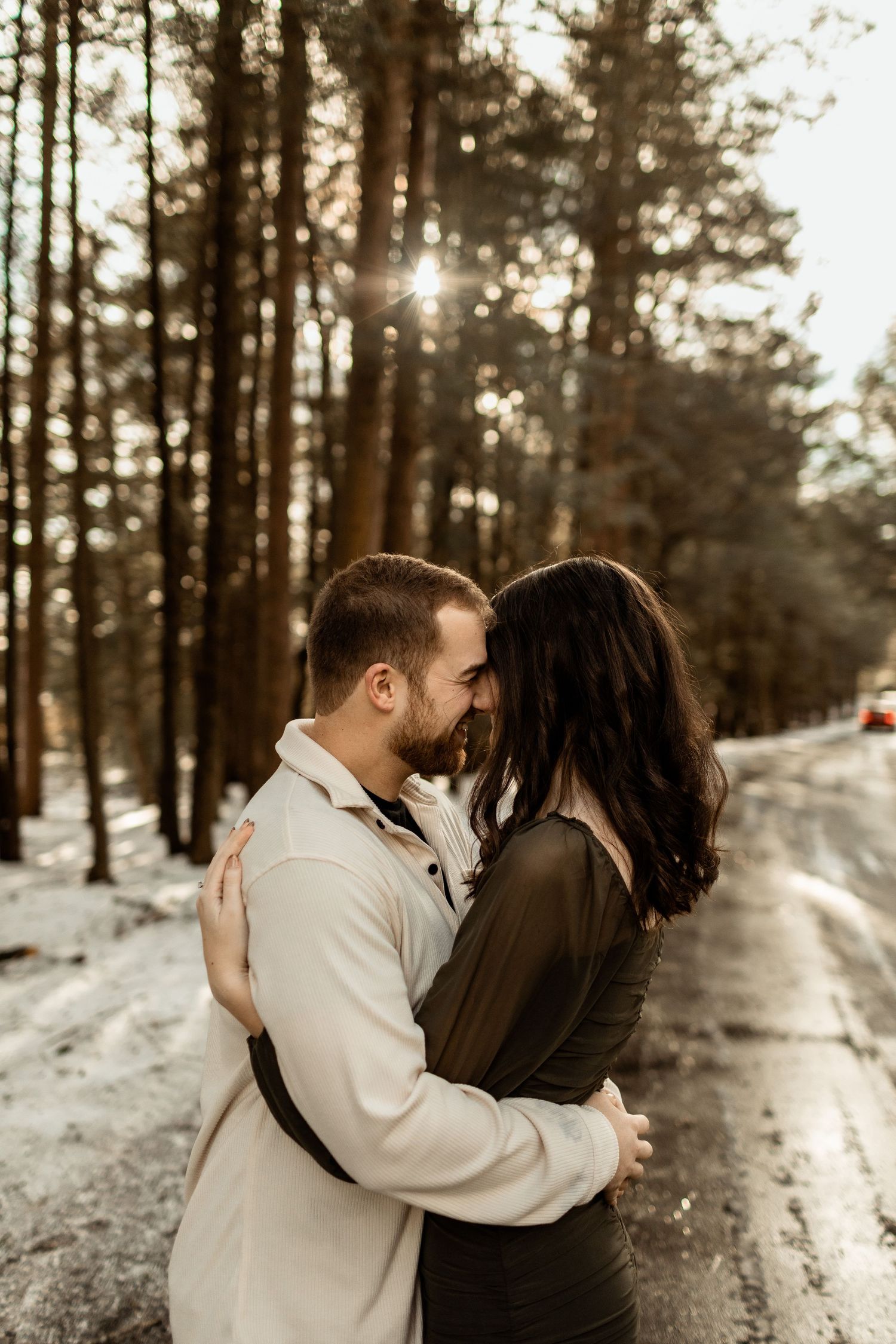 Intimate winter portrait of couple embracing on snowy forest path.