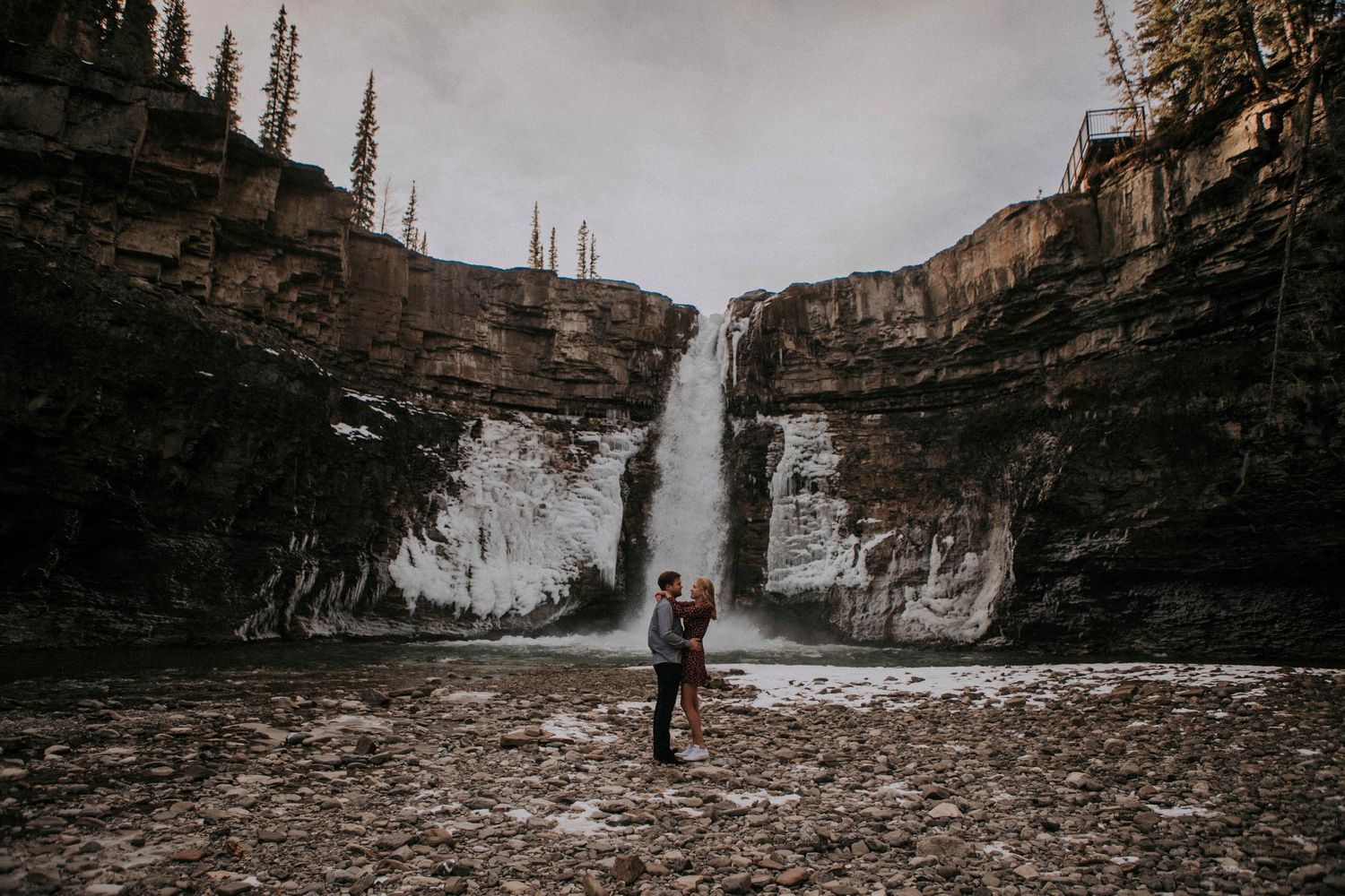 Person standing before a majestic waterfall between towering cliffs.