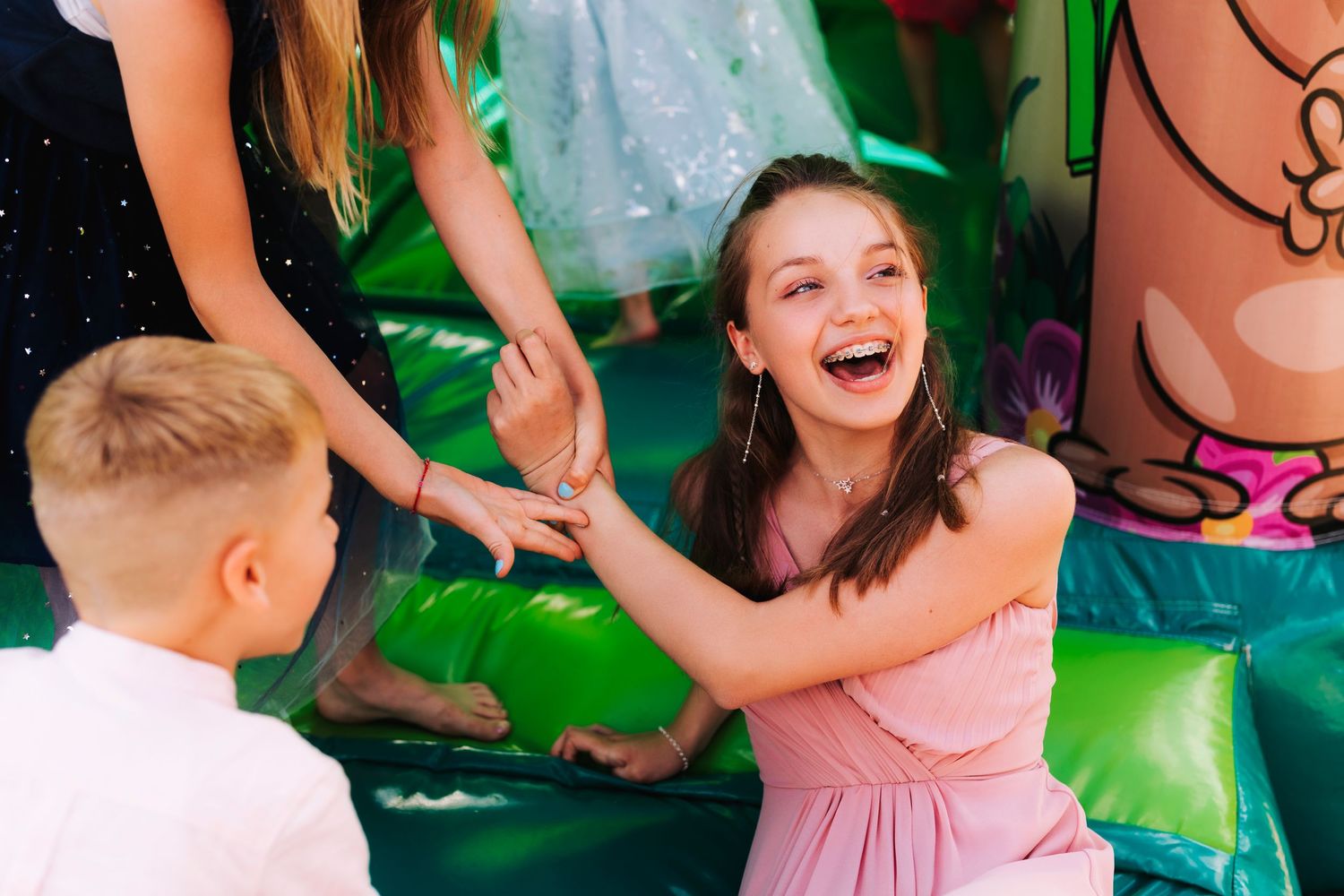 Children playing and having fun in a bouncy castle with green decorations.