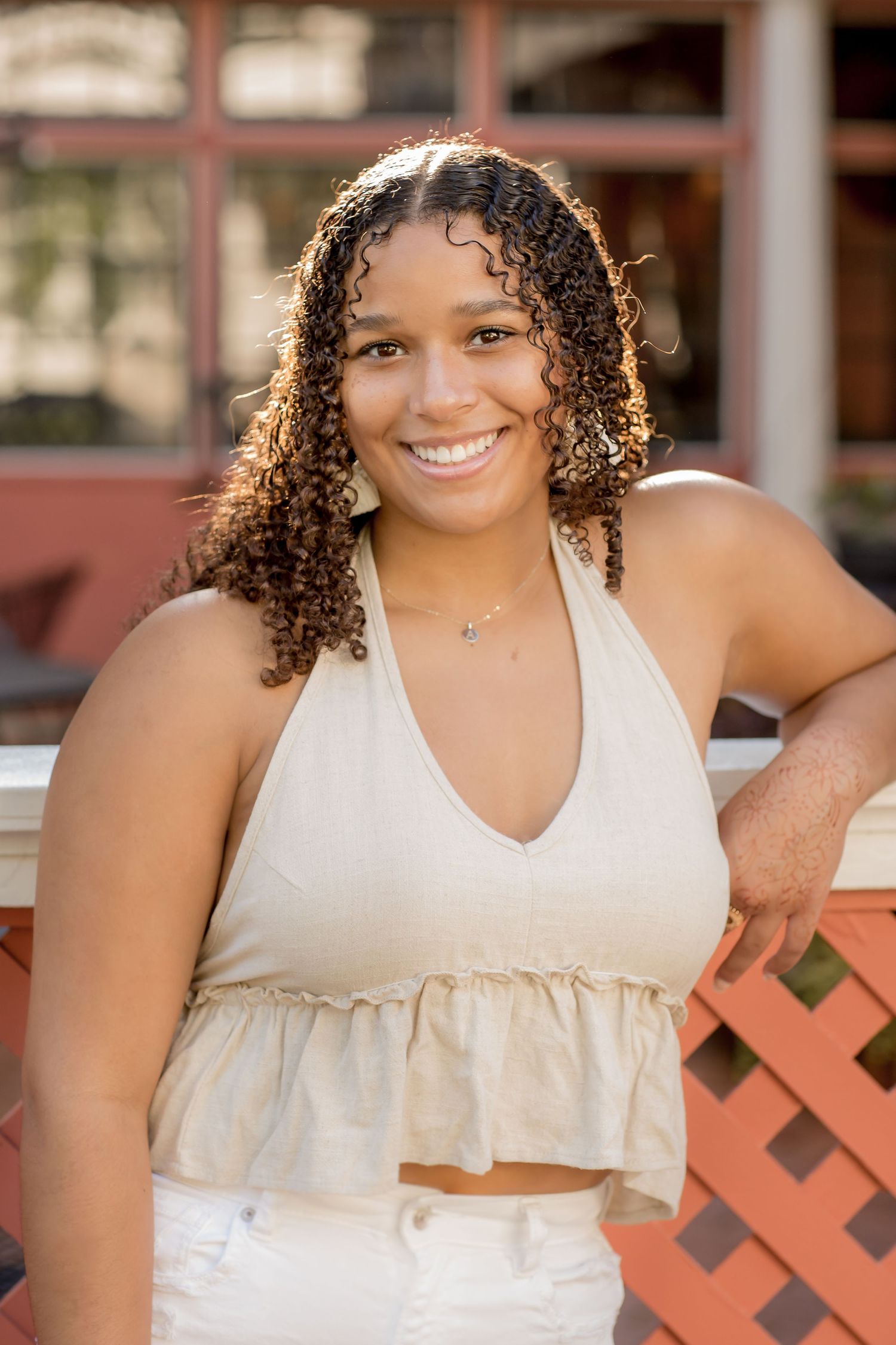 Young woman with curly hair smiling in a beige crop top outdoors.