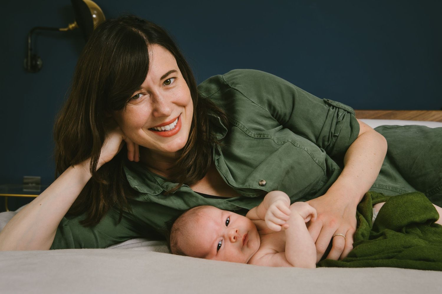 A heartwarming moment showing parent and baby lying together on a bed in casual green attire.