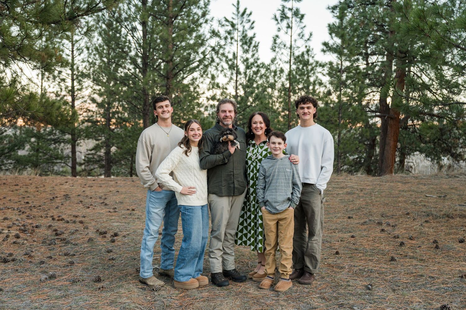 A family poses together on a dirt slope with pine trees in the background at dusk.