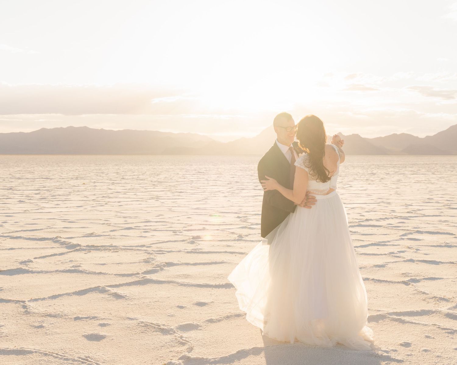 A dreamy sunset wedding portrait on salt flats with mountains in the background.