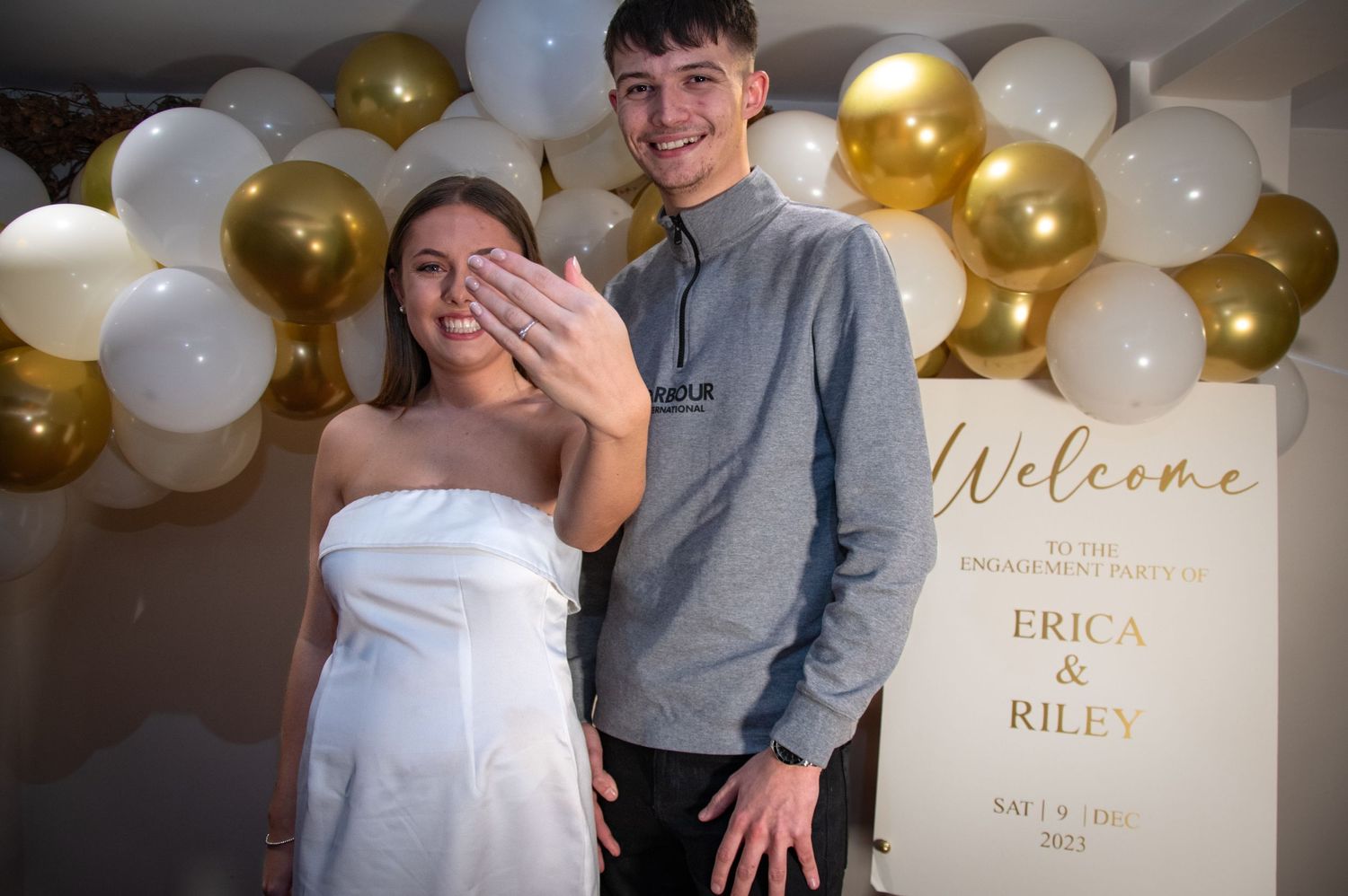A couple shares a joyful moment at their engagement party with gold balloon decorations.