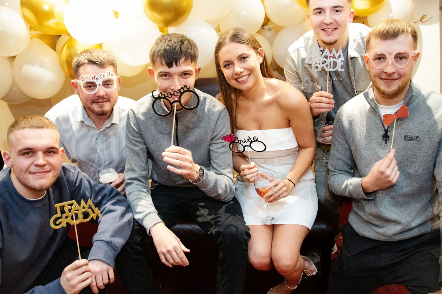 Group celebrates together in front of gold and white balloon wall display.