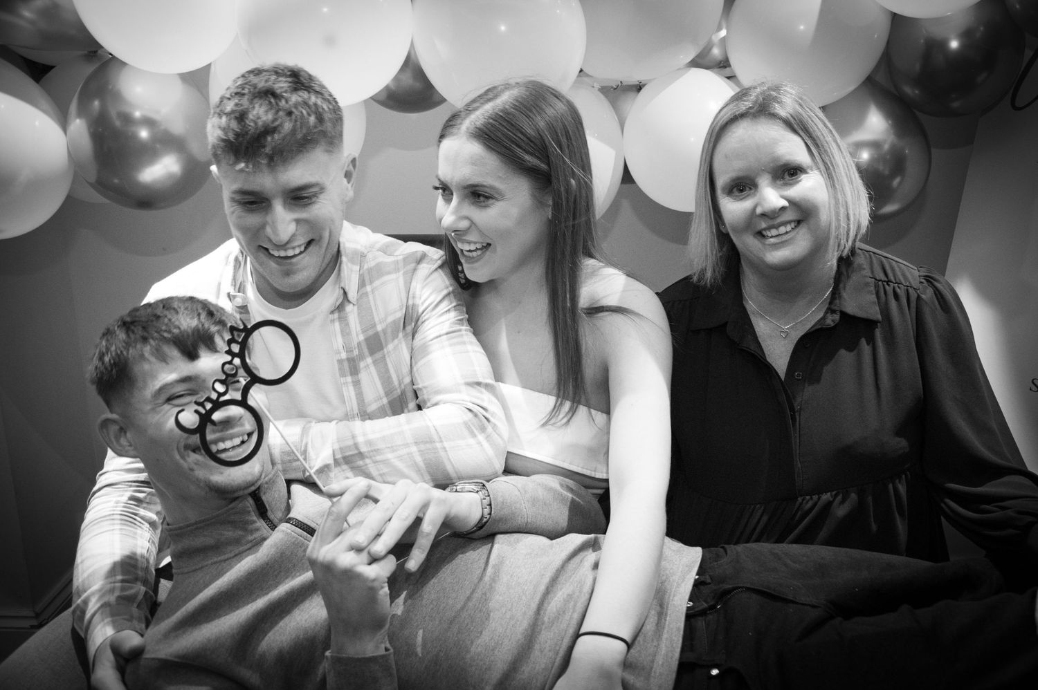 Black and white photo of group gathering with balloons in background.