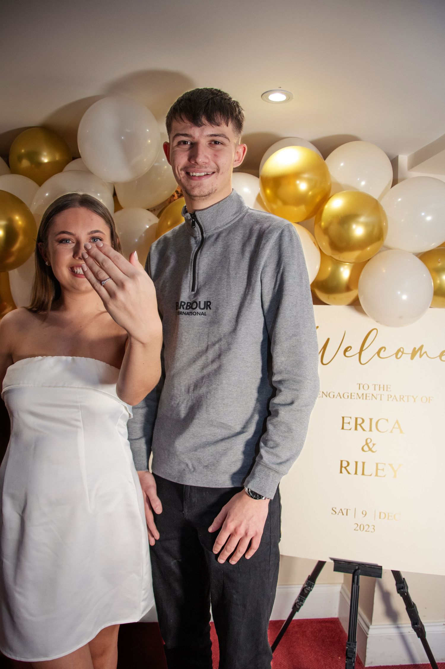 A celebration scene with gold and white balloon decorations and a welcome sign.