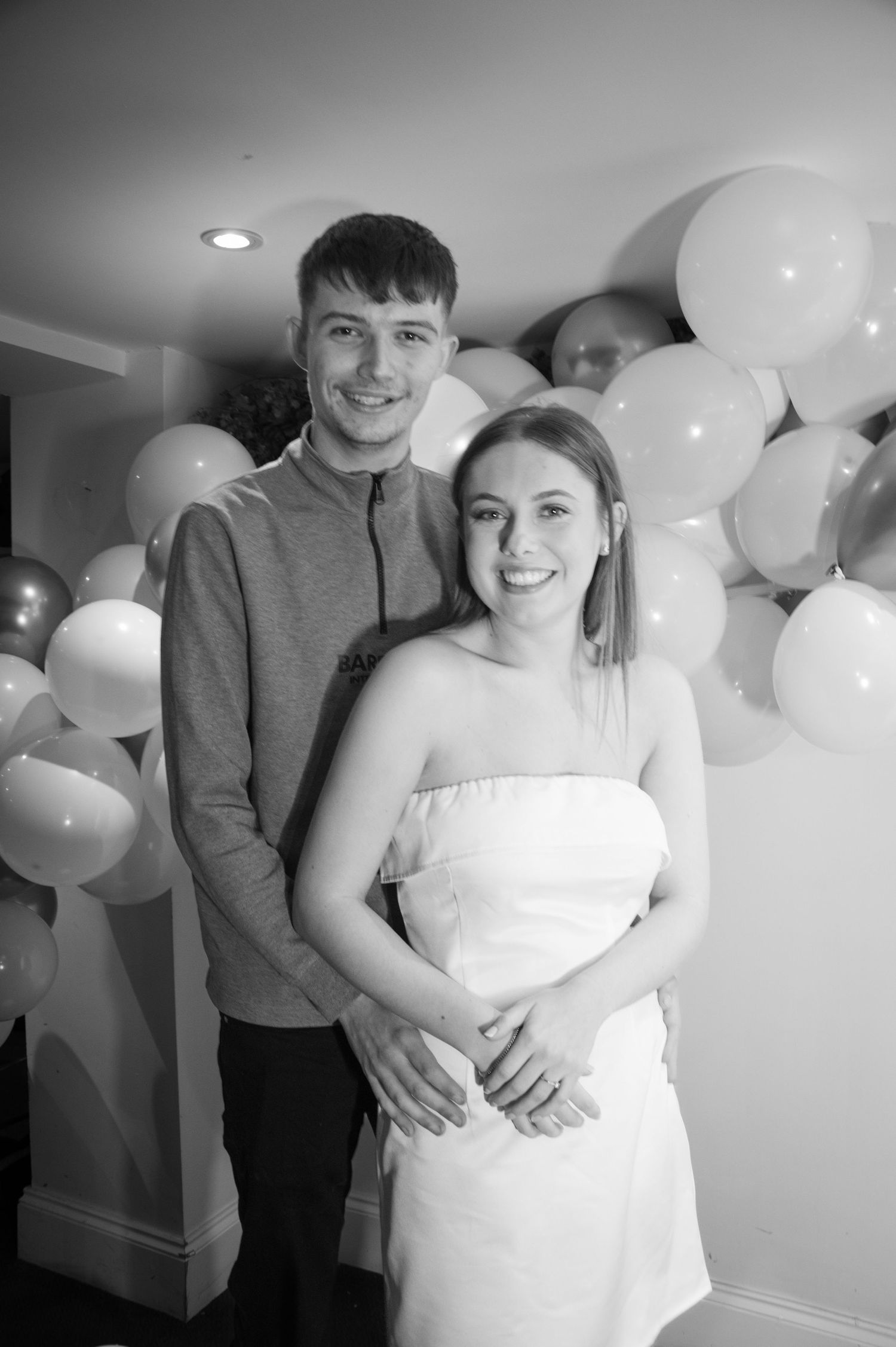 Couple poses in front of elegant white balloon display at celebration event.