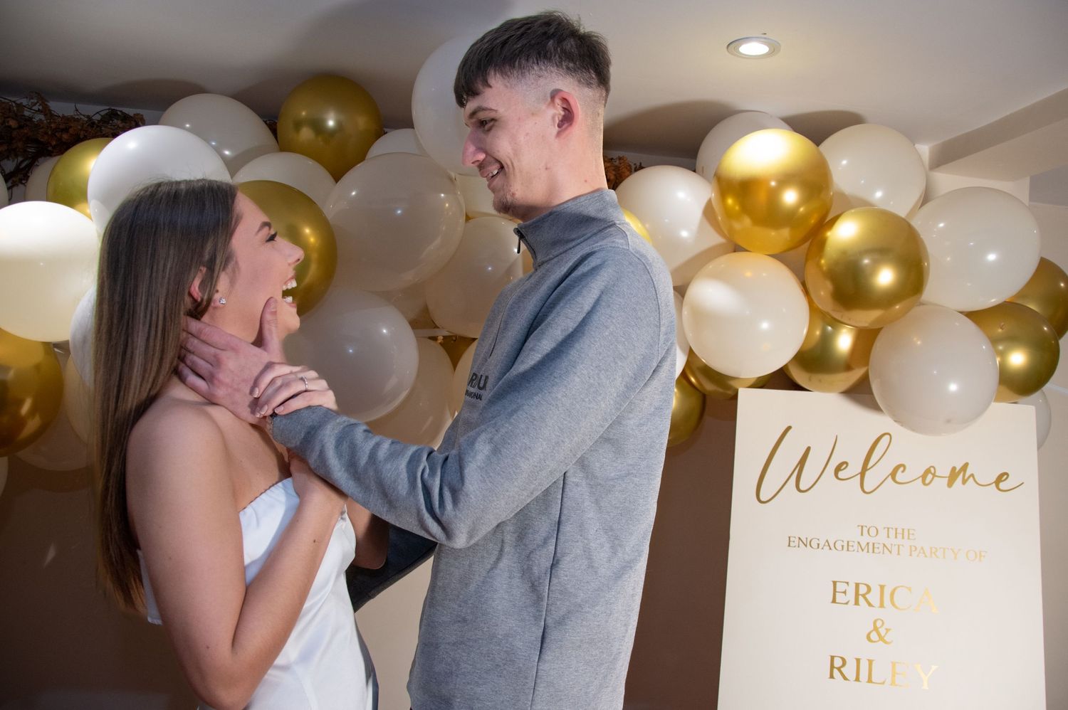 A tender moment between a couple at their engagement party with festive balloon decor.