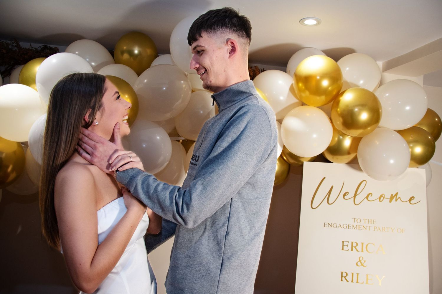 A couple shares an intimate moment in front of a balloon arch and welcome sign.