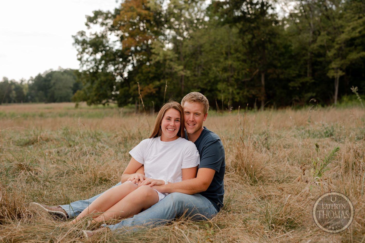 A couple relaxes together in a rustic field setting during golden hour.