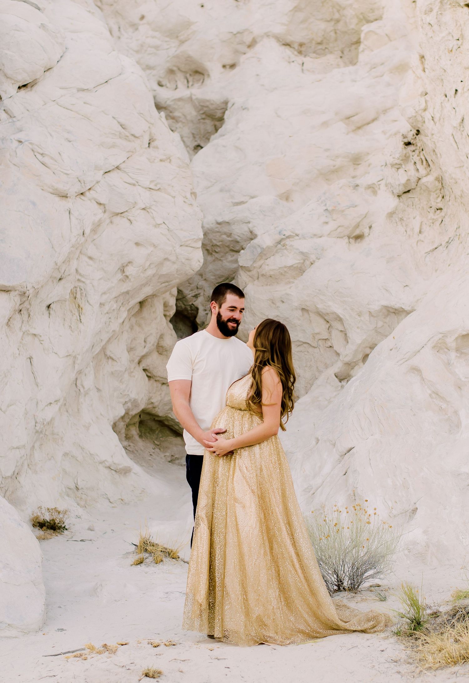 A couple in romantic pose against white limestone cliffs wearing a gold dress and white shirt in desert landscape.