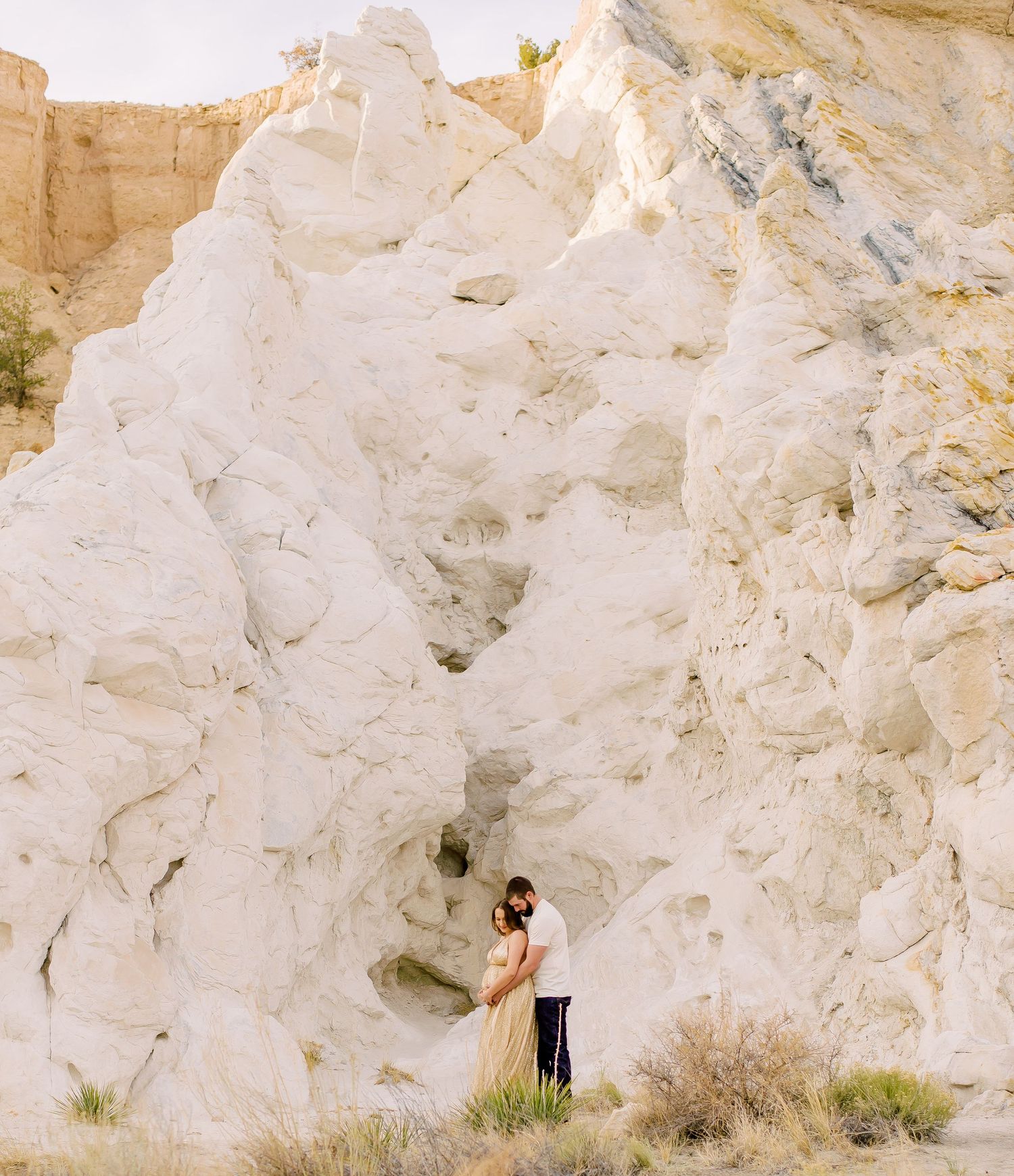 Couple embracing in front of dramatic white rock formation in an arid desert landscape.