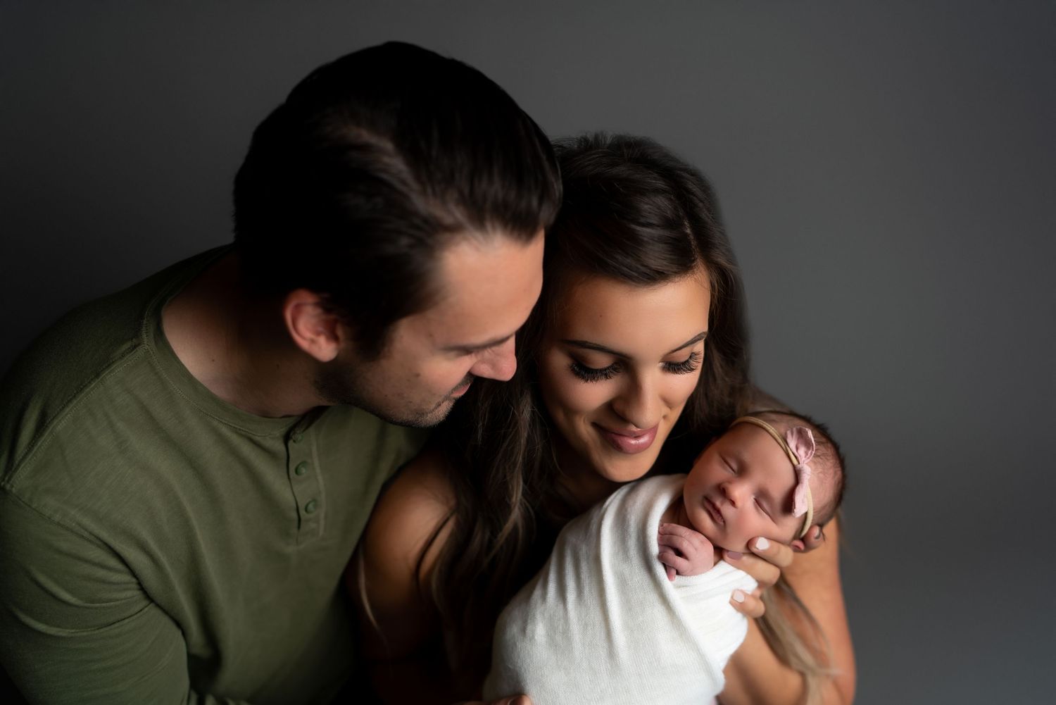 Studio portrait against dark grey background showing tender family moment.
