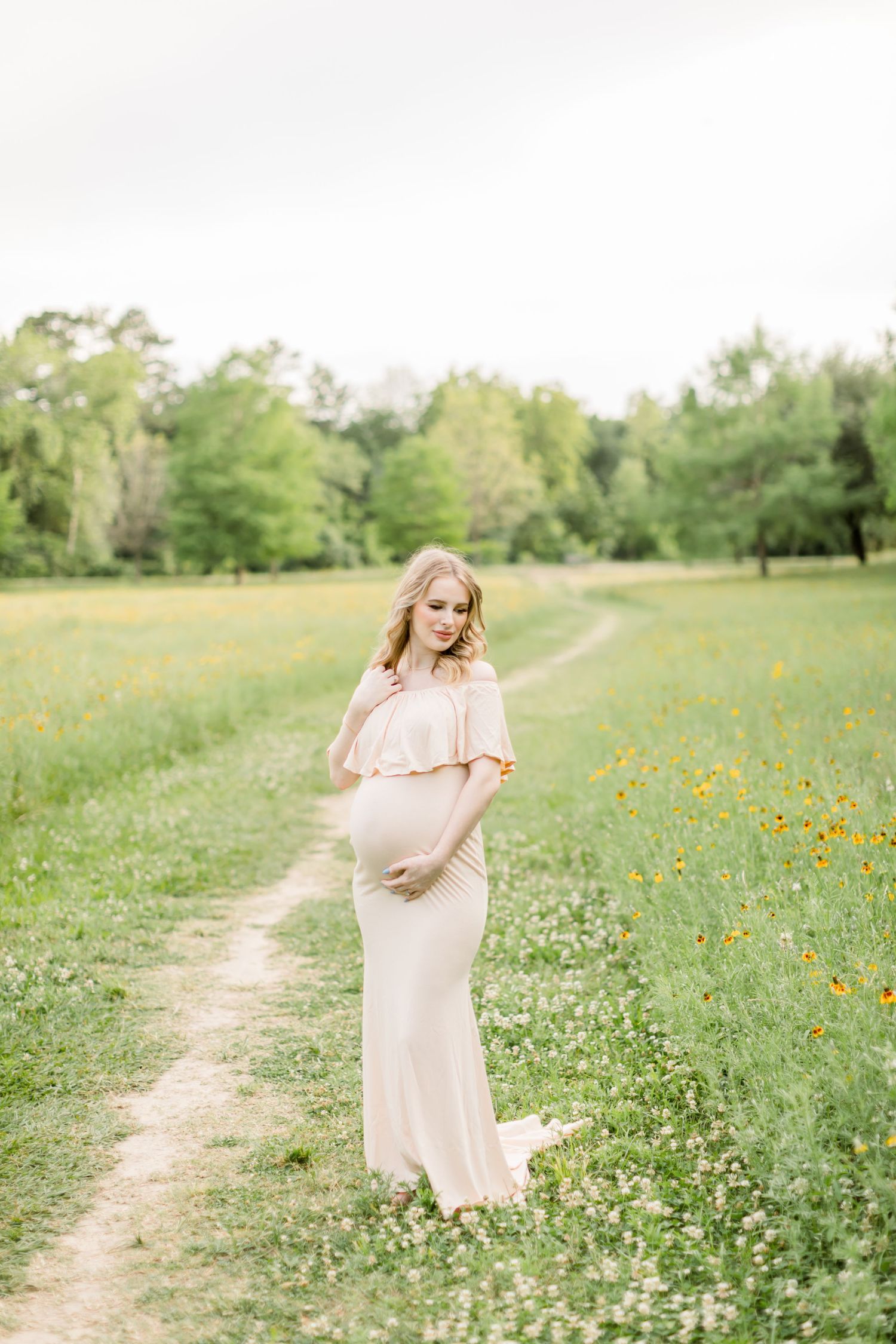 A peaceful maternity portrait in a wildflower meadow with a winding dirt path.