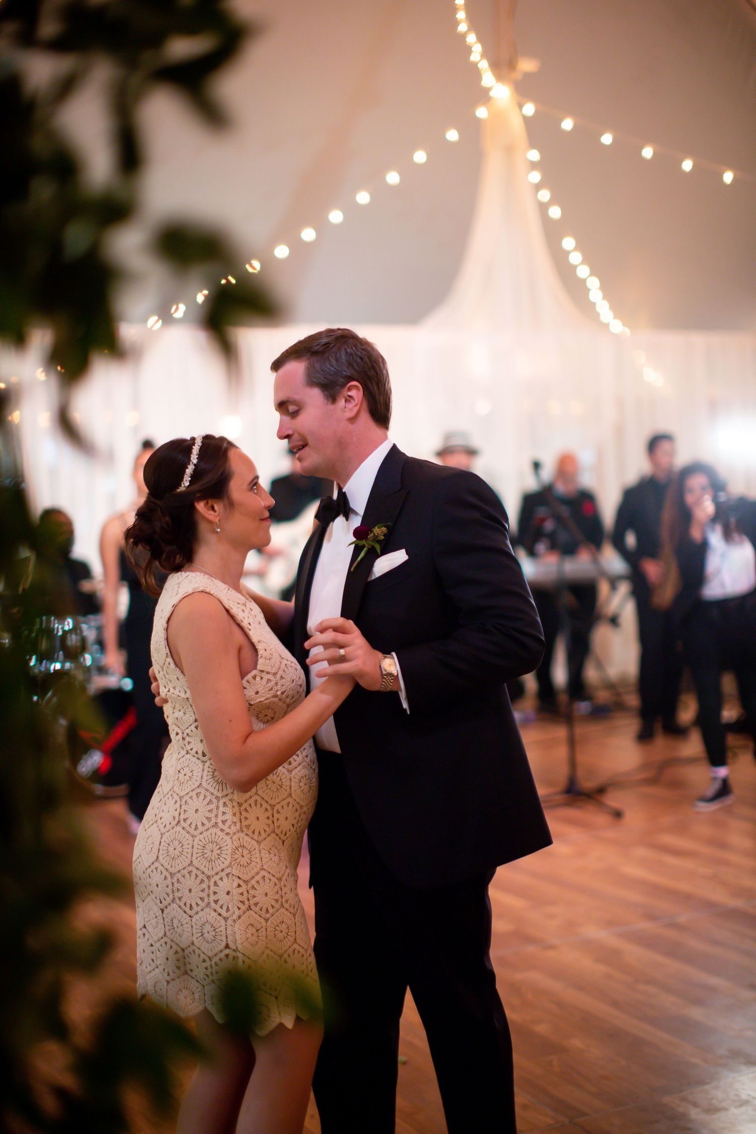 Newlyweds share intimate dance under string lights at reception in elegant tent venue.