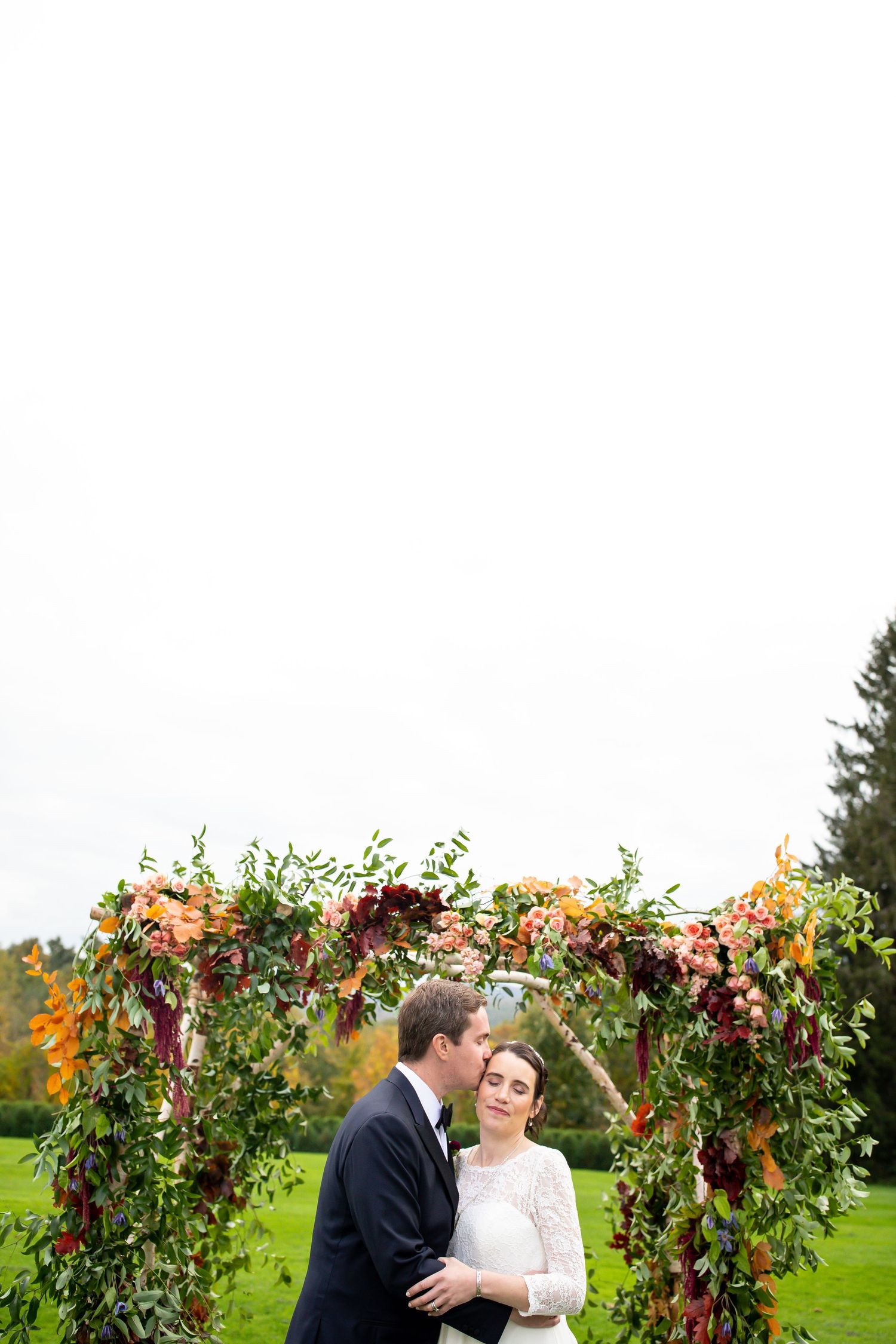 A romantic wedding ceremony arch decorated with autumn foliage and flowers in an outdoor garden setting.