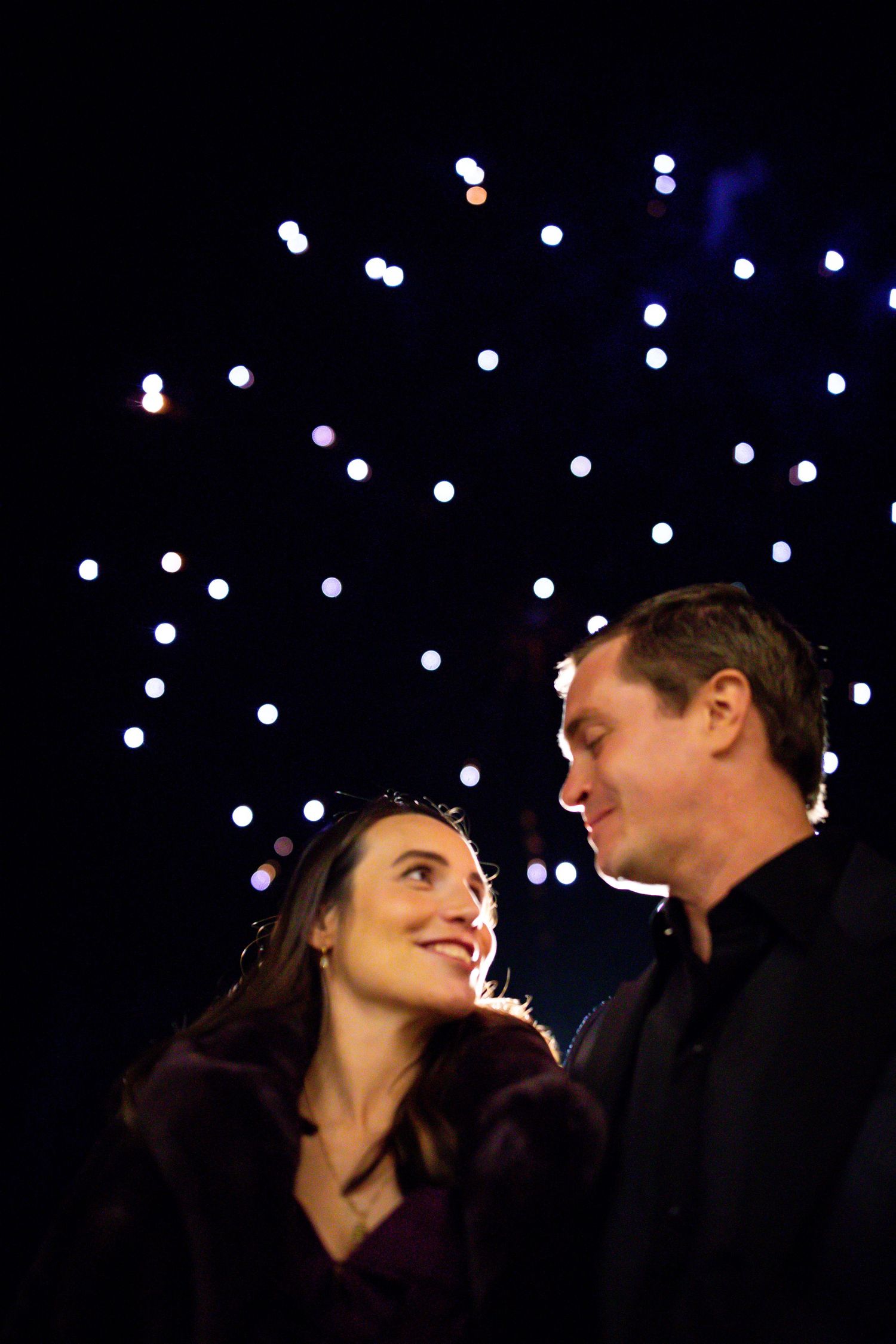 A romantic nighttime portrait with twinkling lights creating a starry backdrop.