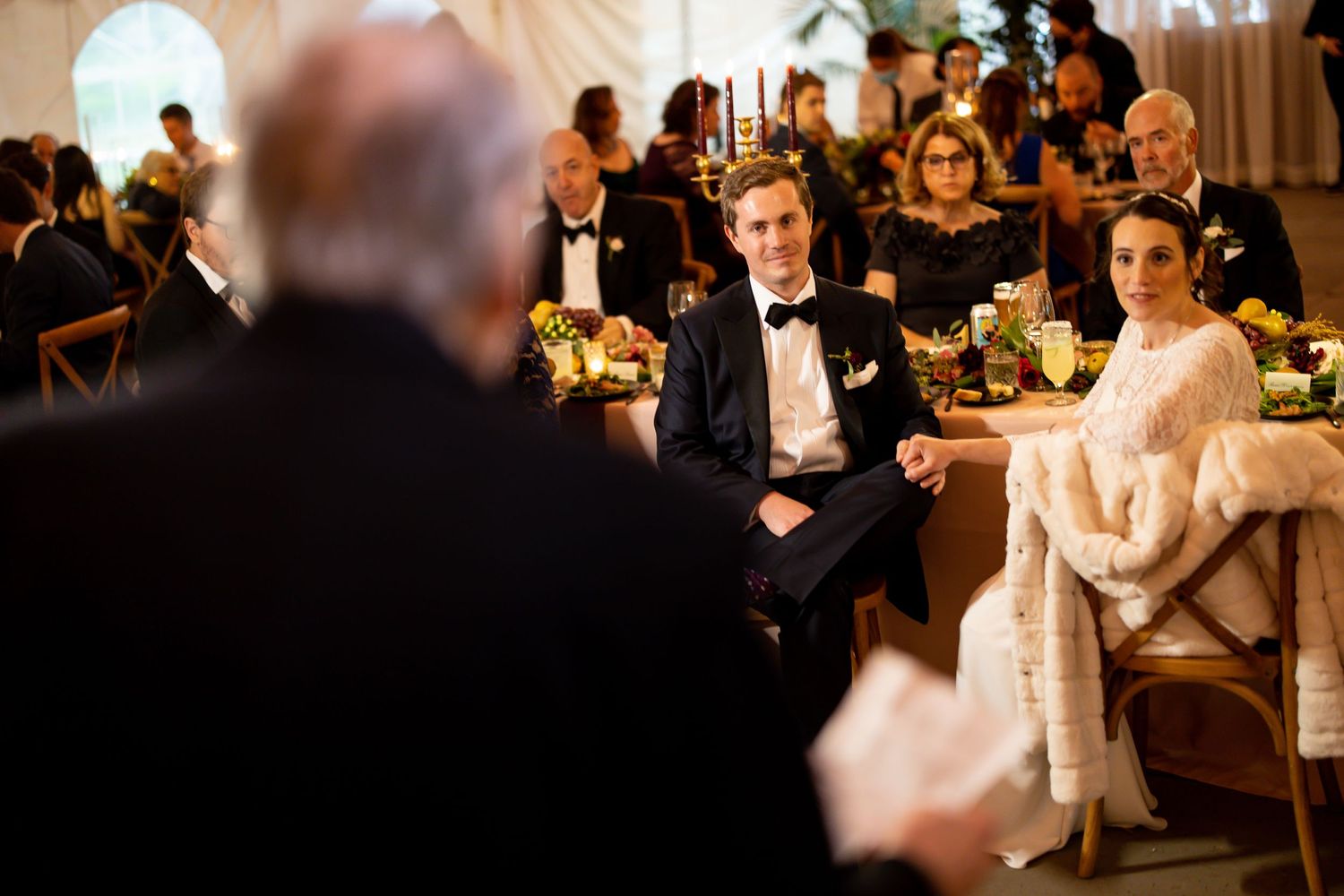 A wedding reception scene showing guests seated at elegantly decorated tables with floral centerpieces.