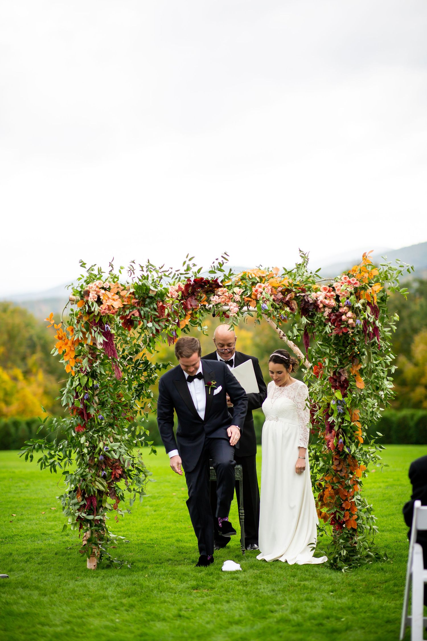 A beautiful autumn wedding ceremony under a lush floral arch with orange and burgundy blooms.