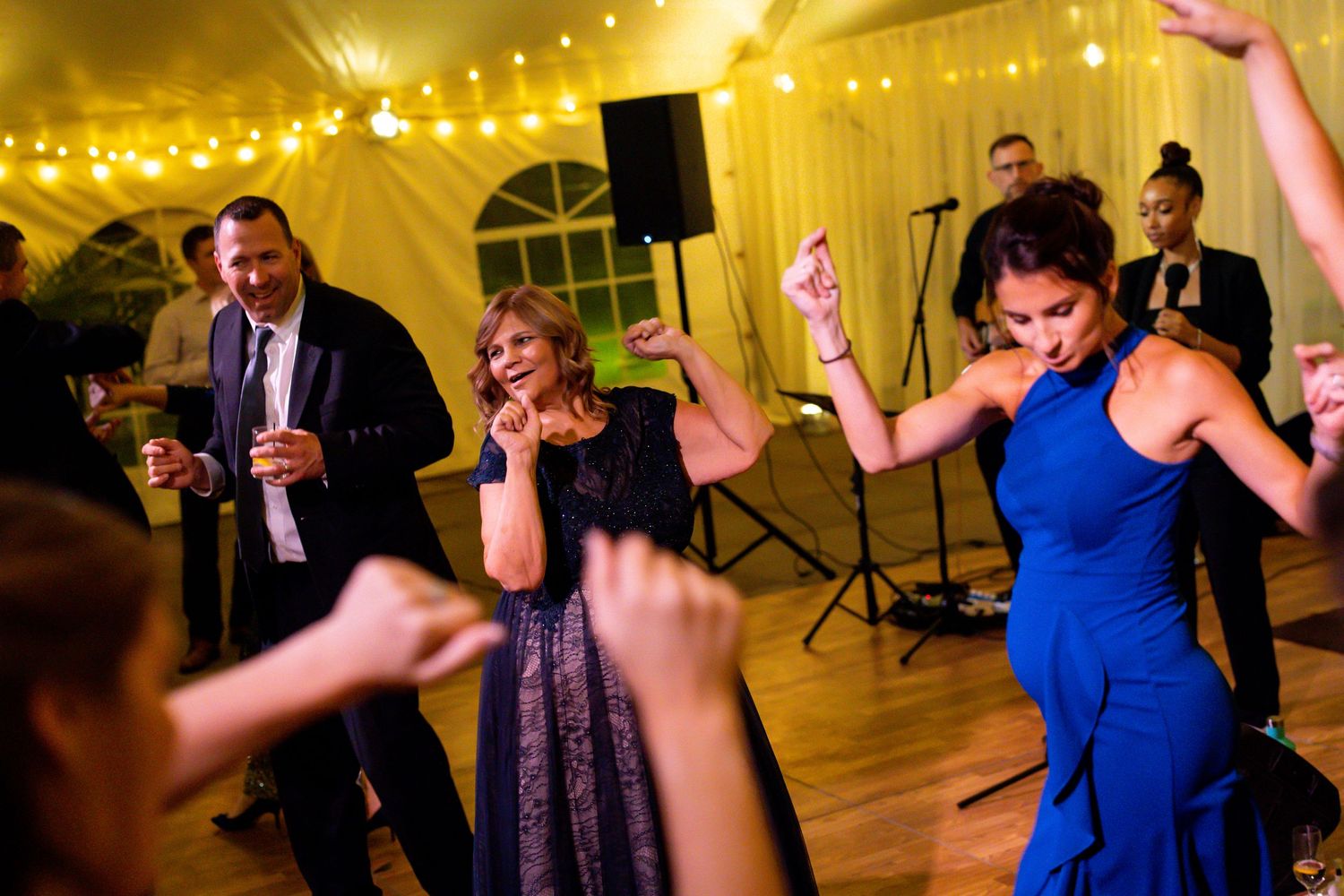 Wedding guests dancing energetically under yellow tent lighting at an evening reception.