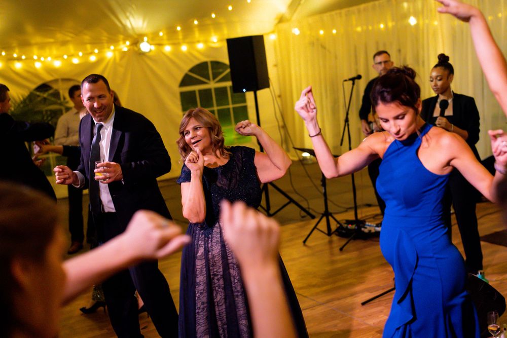 Wedding guests dancing energetically under yellow tent lighting at an evening reception.