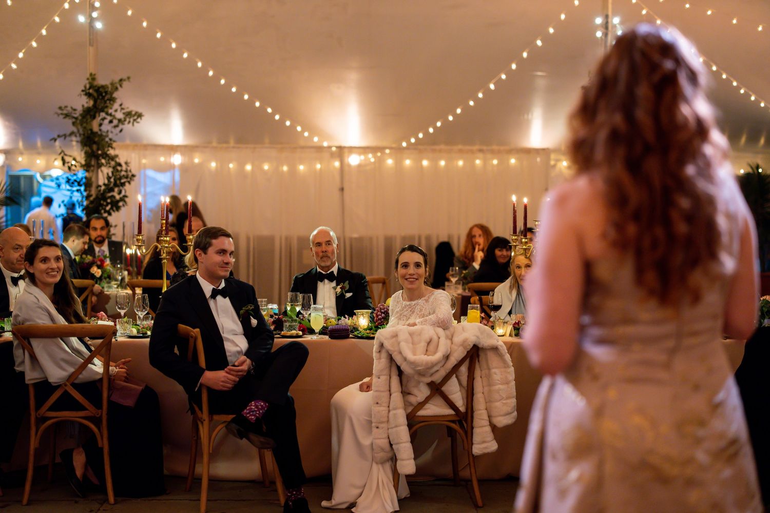 An elegant tented wedding reception with string lights and guests seated at decorated tables.