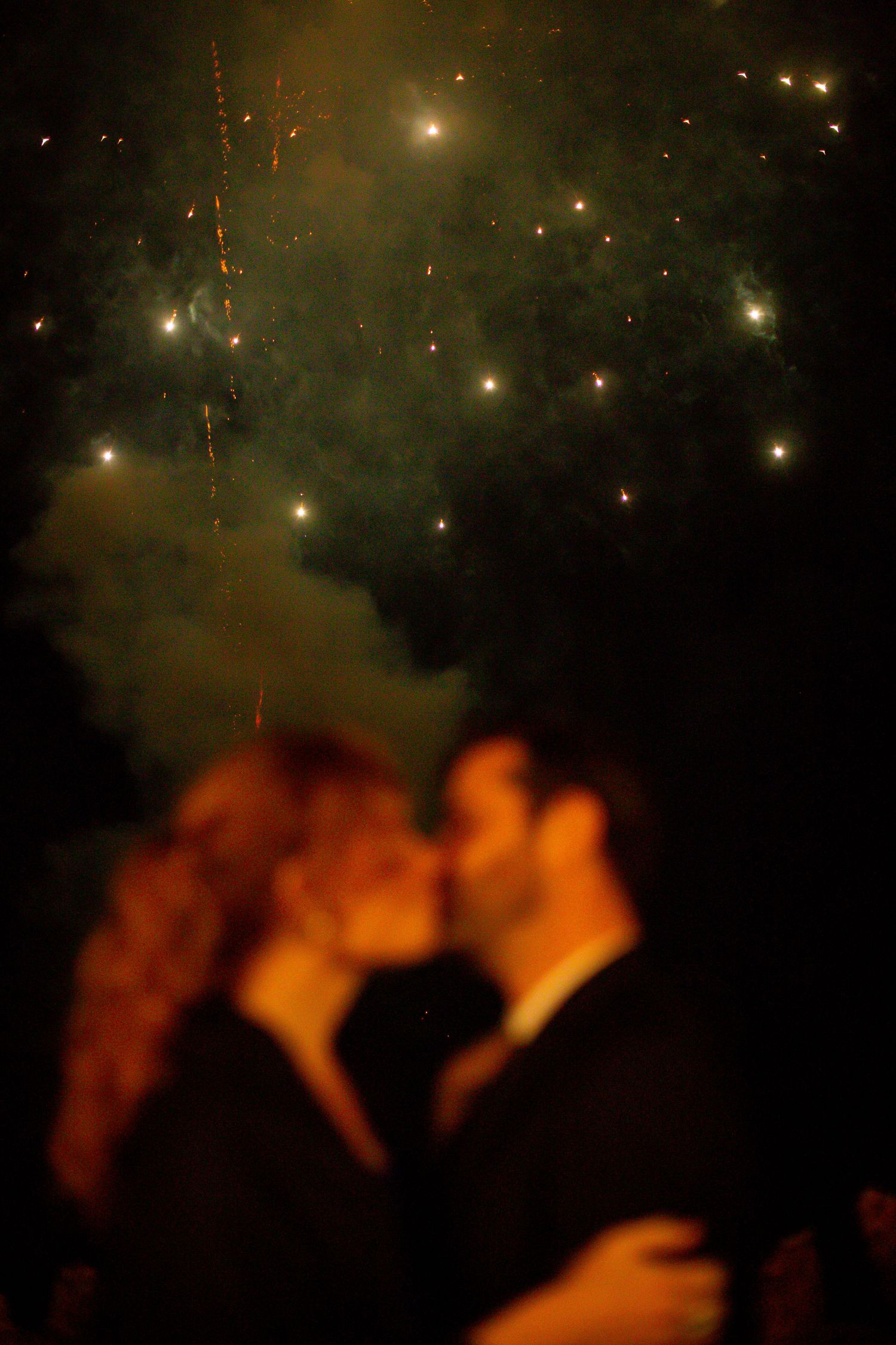 Fireworks illuminate the night sky with sparkling gold and green bursts against dark silhouettes.