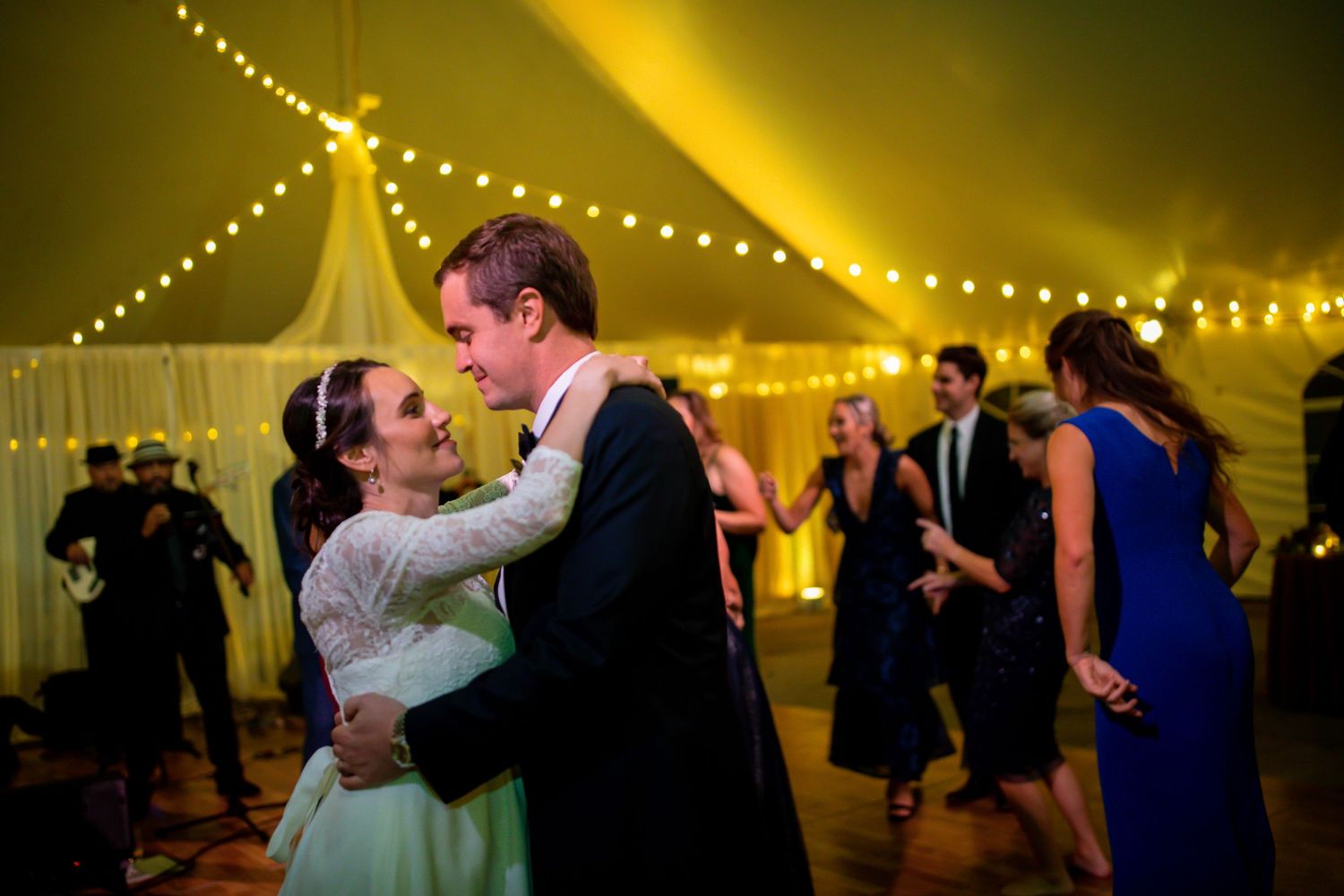 A joyful dance moment captured under warm string lights in a wedding reception tent.