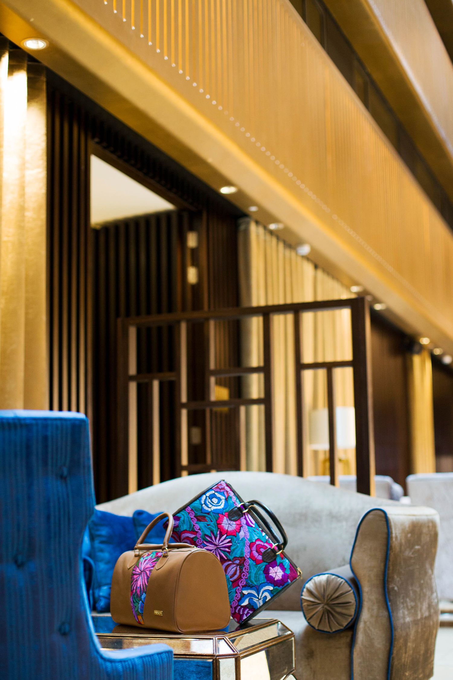 Stylish floral print handbags arranged on luxury furniture with blue velvet upholstery.
