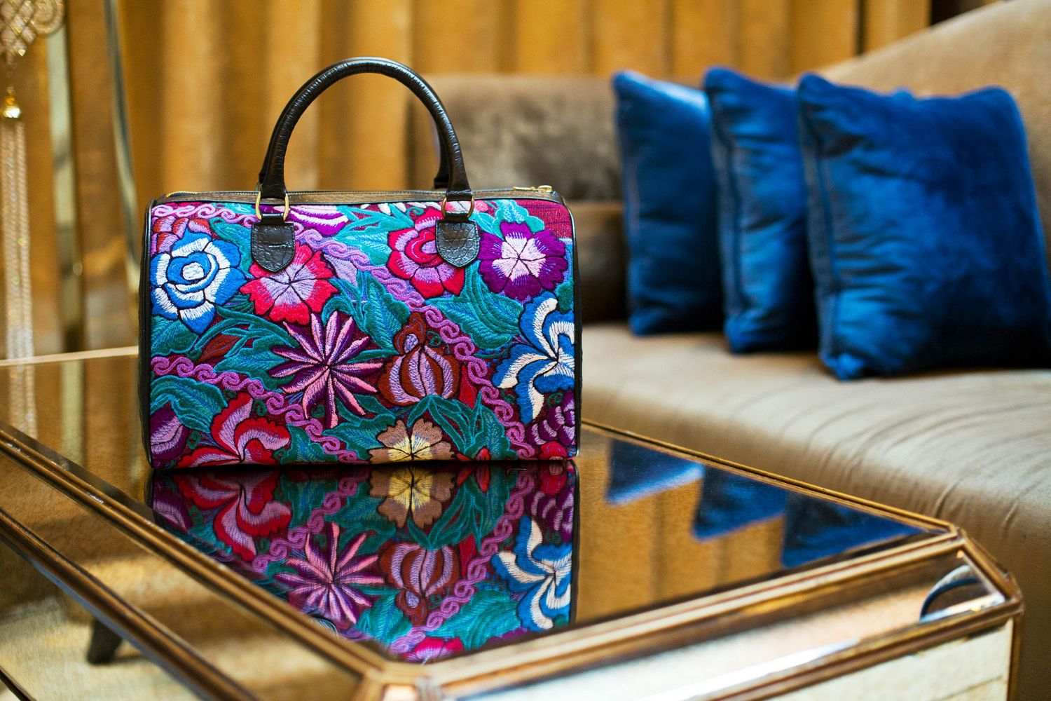 Floral patterned handbag with bright pink and blue flowers reflected on mirrored table surface.