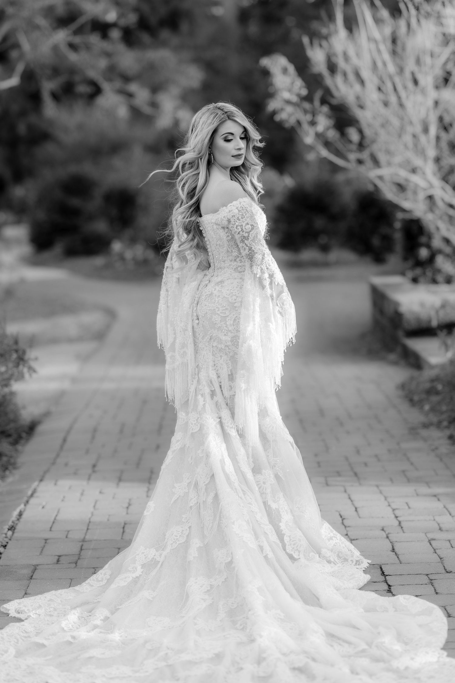 Black and white portrait of a bride in a lace wedding gown with flowing train.