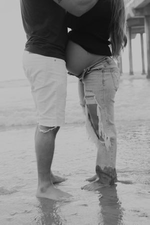 Two pairs of legs standing in shallow beach water wearing ripped jeans.