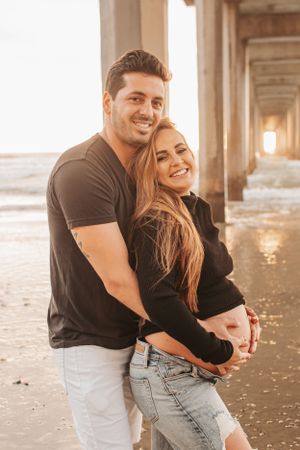 Happy couple sharing intimate moment under pier at sunset.