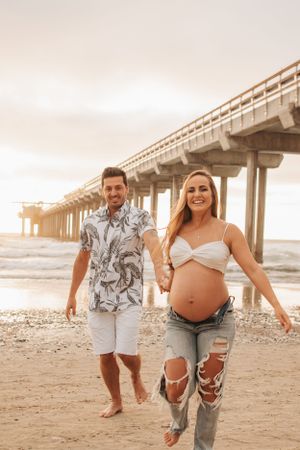 Couple enjoying carefree moment while walking under beach pier at sunset.