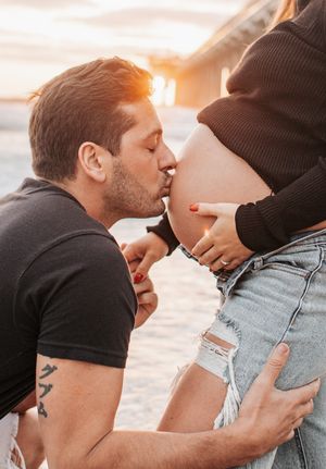 Intimate maternity photo at sunset with tender moment by pier.
