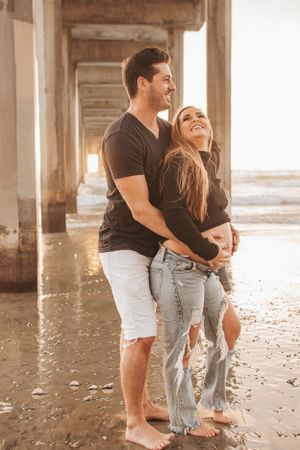 Couple embracing under beach pier during golden hour.