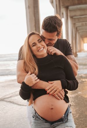 Joyful moment between couple during beachside maternity photography session.