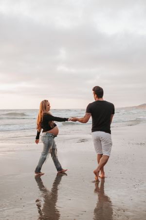 Couple dancing in shallow tide waters on beach during sunset photoshoot.