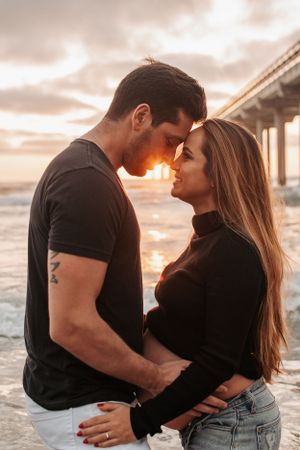 Romantic sunset portrait of couple embracing by oceanside pier.